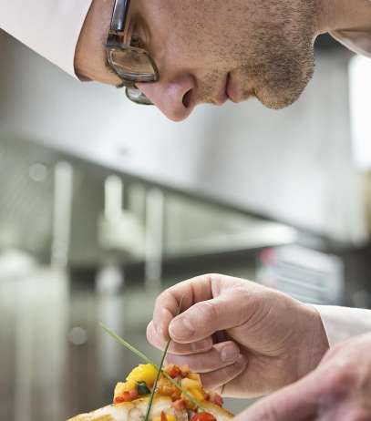 A caucasian male chef putting the finishing touches on a plate of fish in a commercial kitchen.